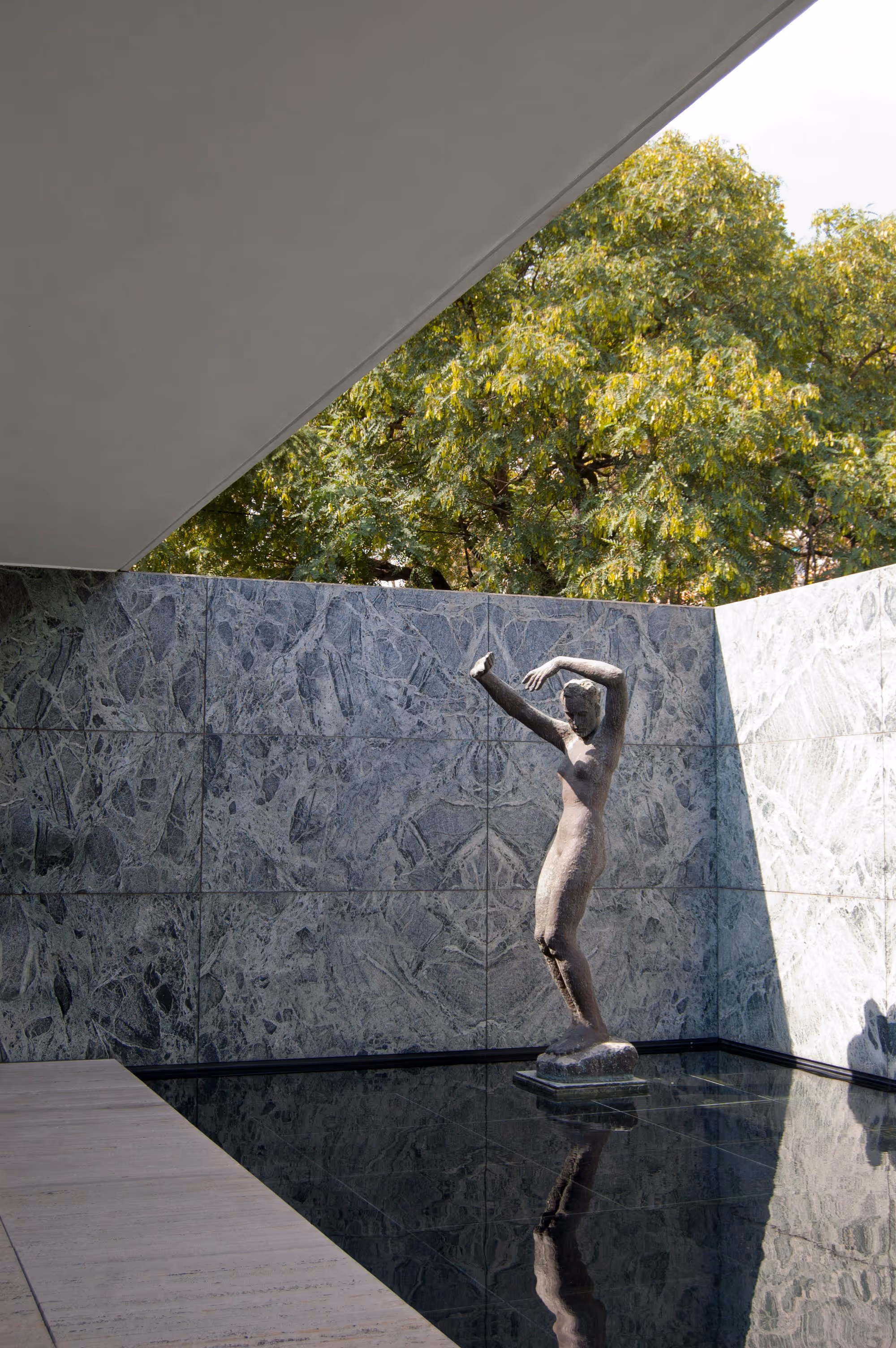 A contemporary statue outside of modern building on water feature with trees in the background