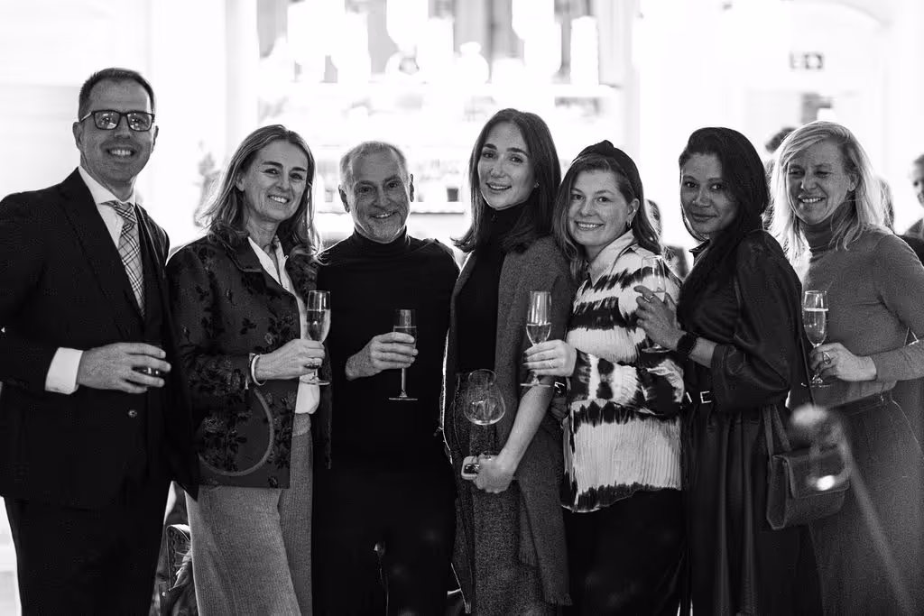 Group of smartly-dressed people smiiling with champagne in hand and luxury interiors in the background
