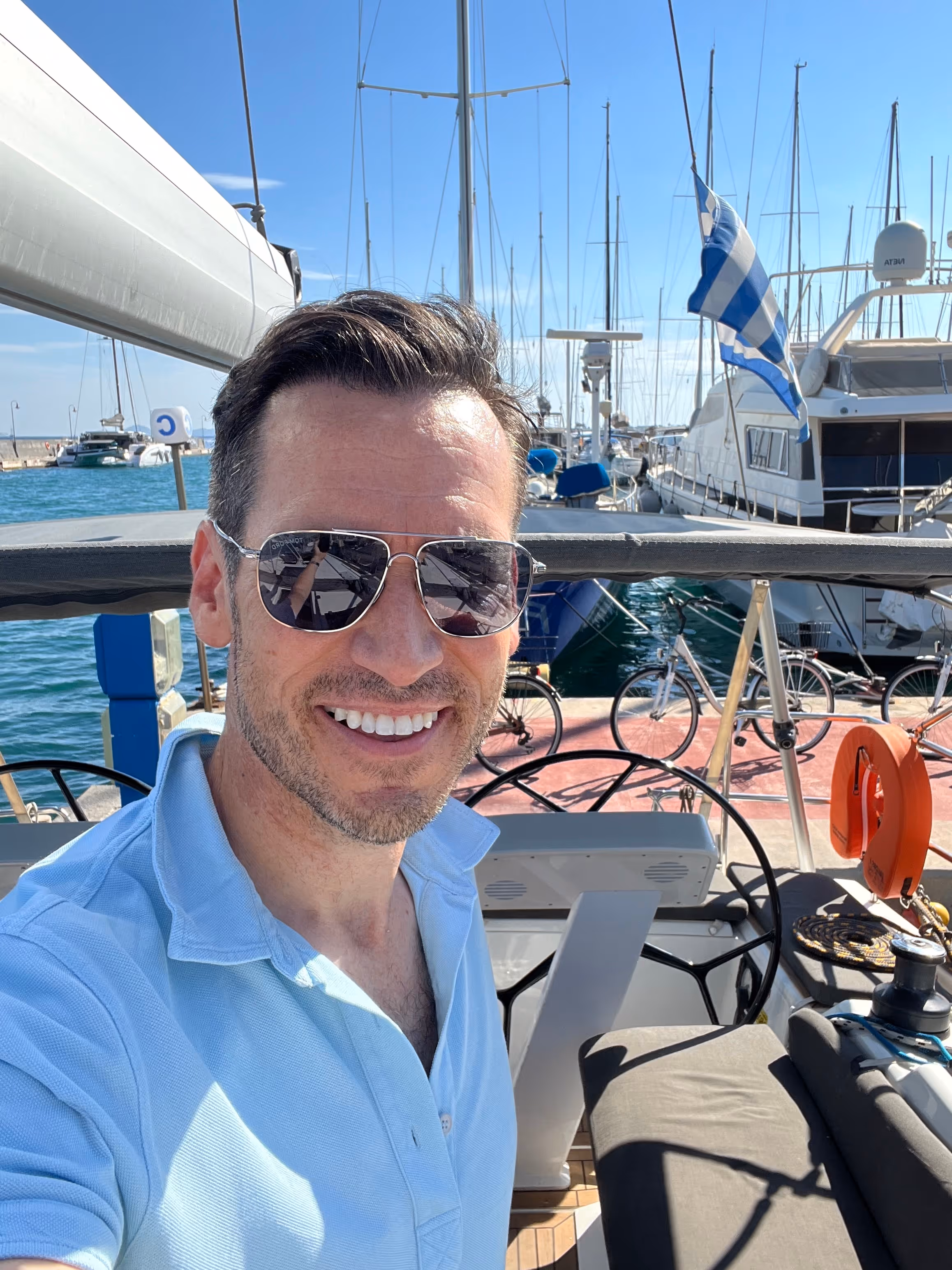 Selfie of man with brown hair smiling in front of boat dock with blue skies