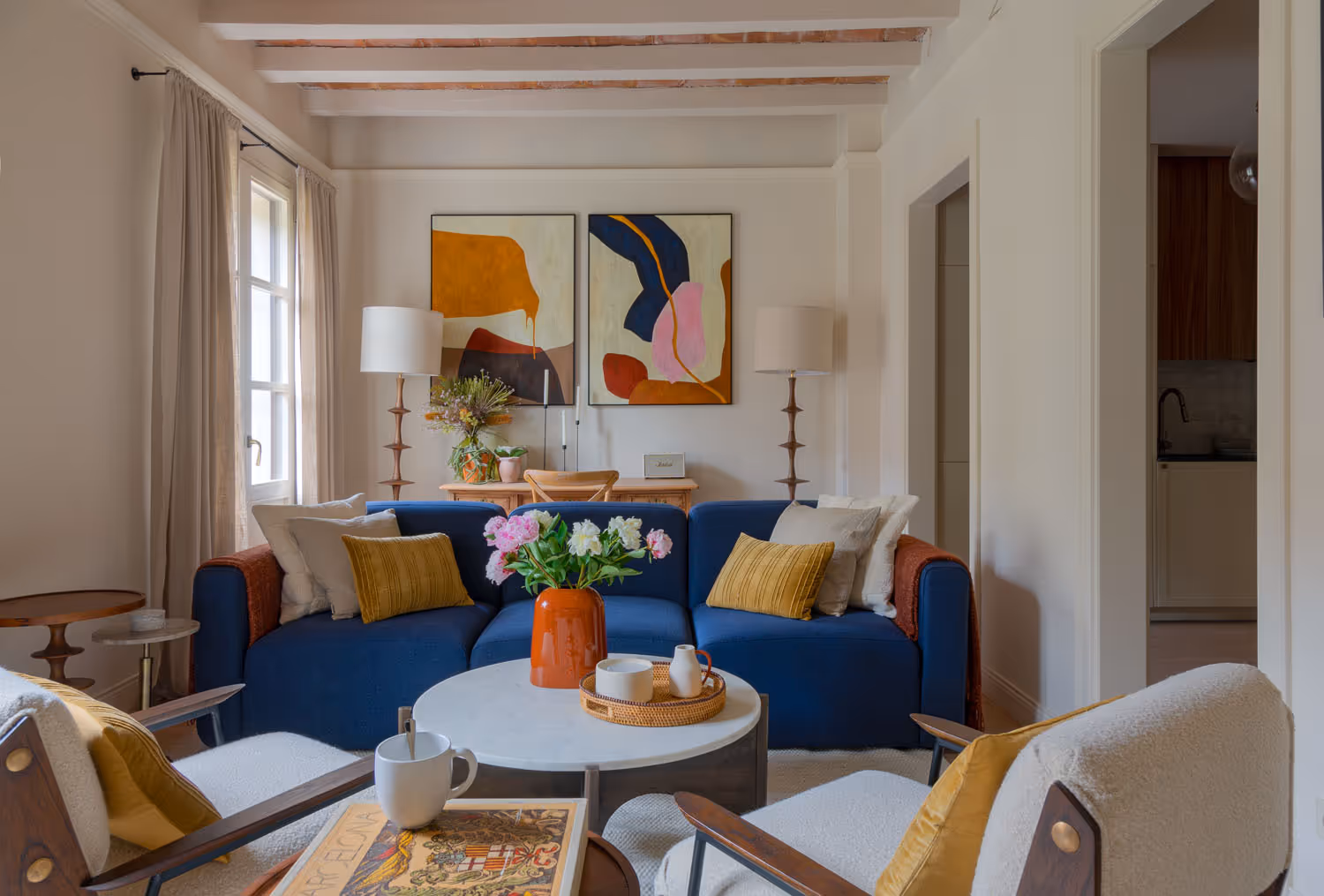 White living room space with colourful and eclectic decorative additions, a blue couch, flowers and abstract art on the wall