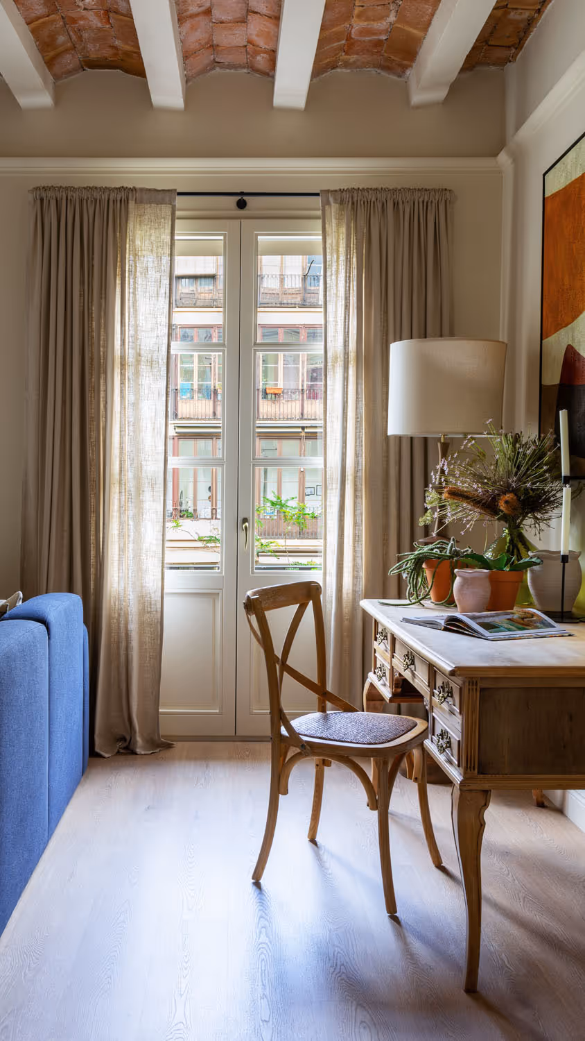 Desk space near window in room with exposed brick between white painted wooden beams