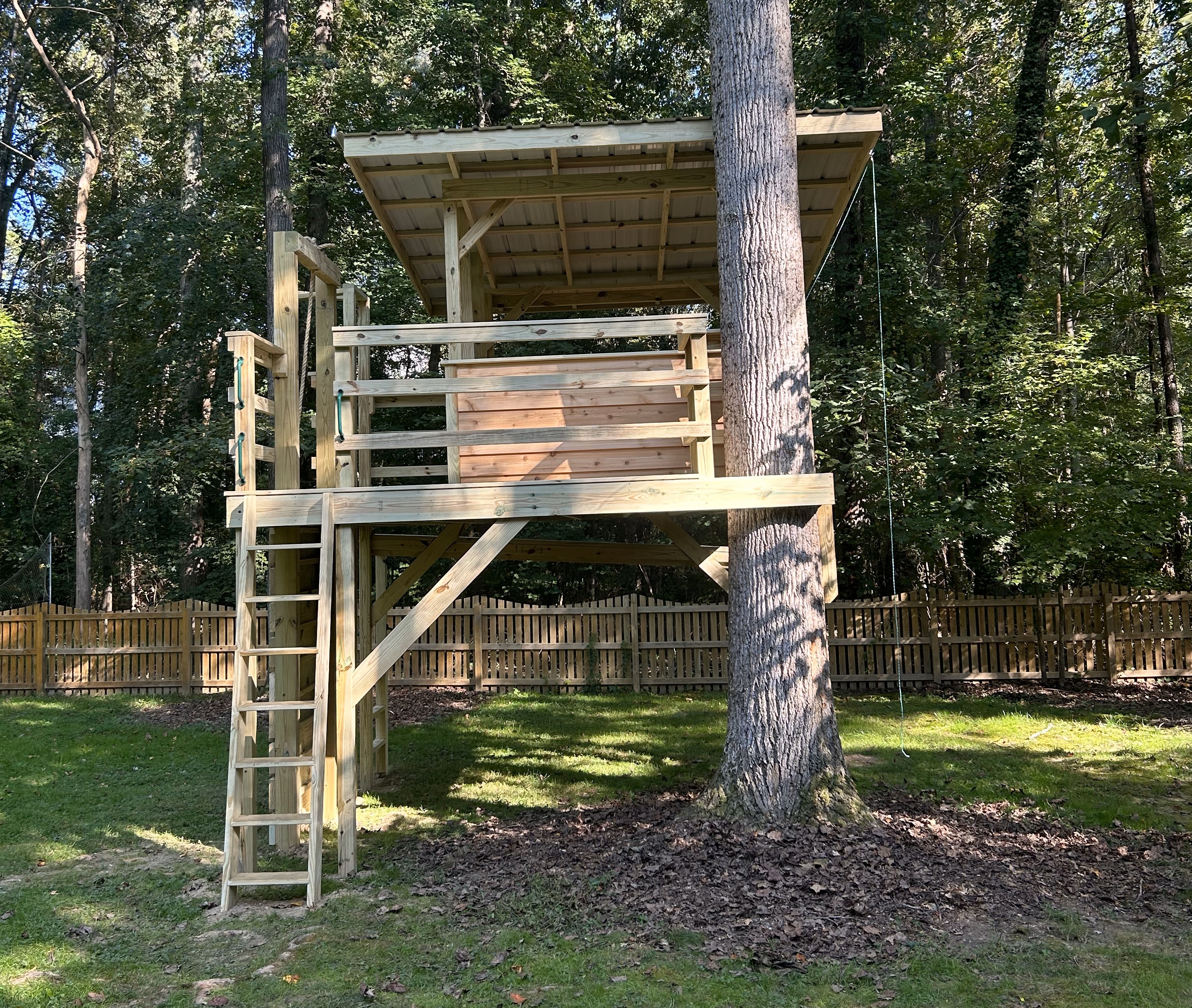 Treehouse with grab handles. Tree is encased in wooden cross beam of tree house. Ladder and rope swing.