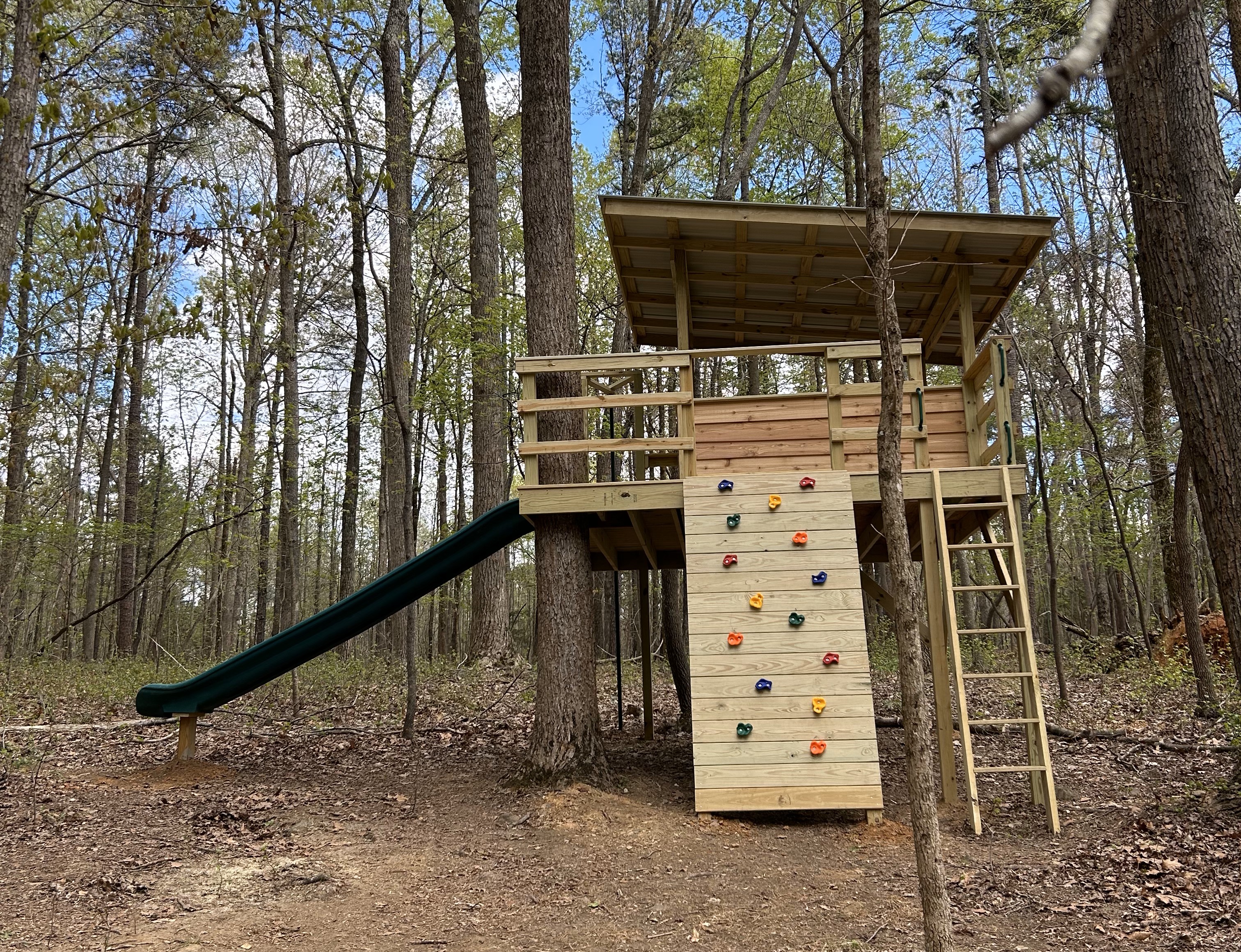 Colorful climbing holds on the climbing wall, deck with a roof, ladder and green slide.
