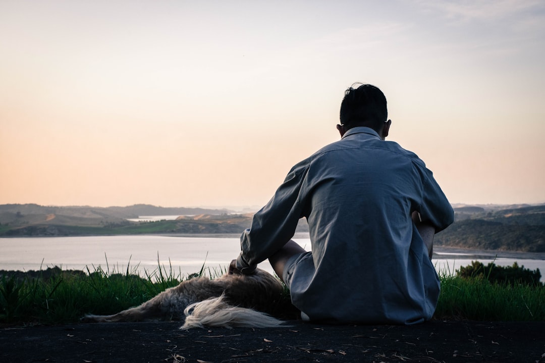 man in gray hoodie sitting on black rock near body of water during daytime