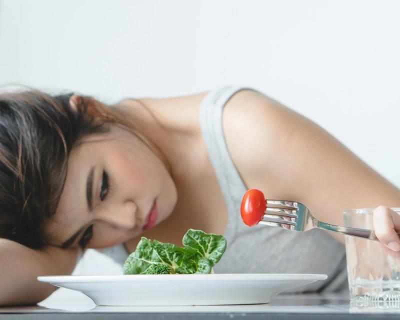 Woman looking discouraged while eating a salad, expressing frustration with restrictive dieting