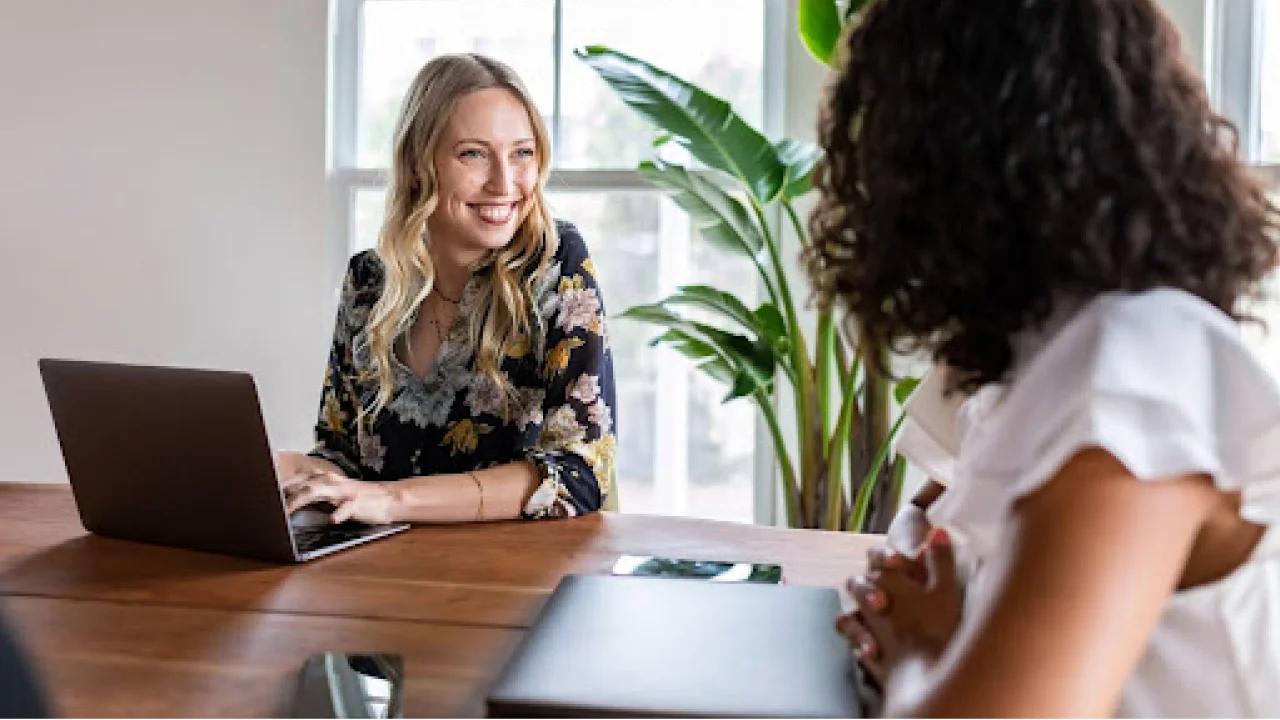 A leader having a one-to-one meeting with their team member in a sunny office.