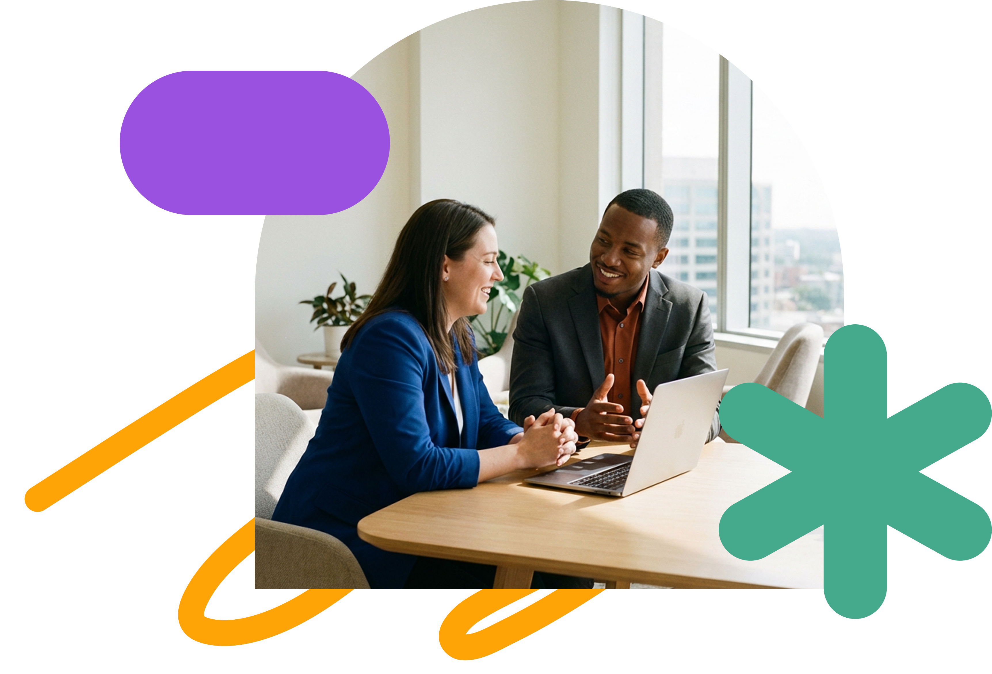 Two colleagues sit together at a table in a bright office, smiling and talking while looking at a laptop during a one-to-one conversation.