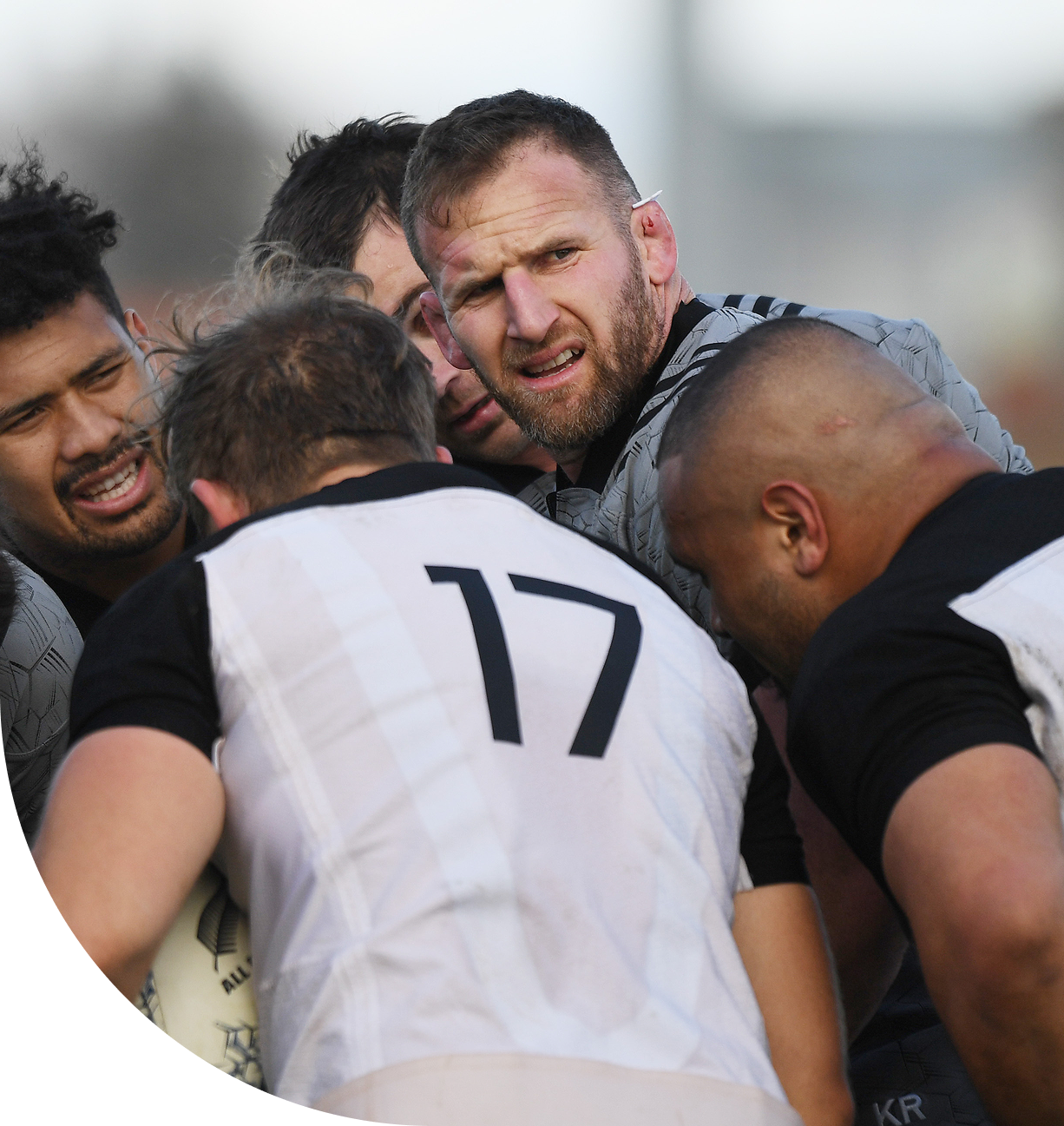 Five rugby players in a close huddle, one holding a rugby ball wearing number 17 jersey.