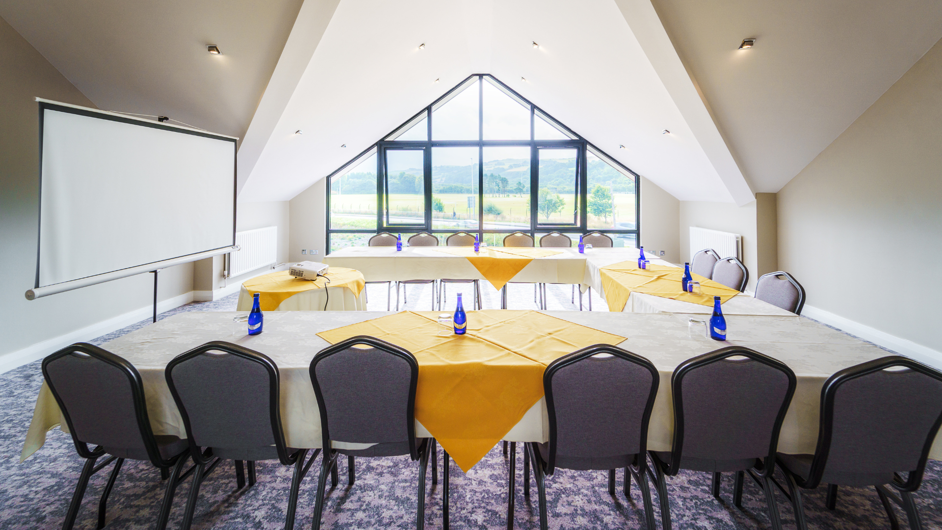 Meeting room set up with tables, chairs and projector screen