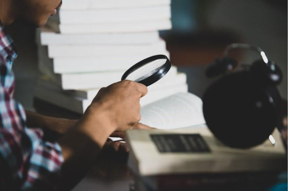 Person using a magnifying glass to closely inspect official documents, symbolizing manual document verification and fraud detection.