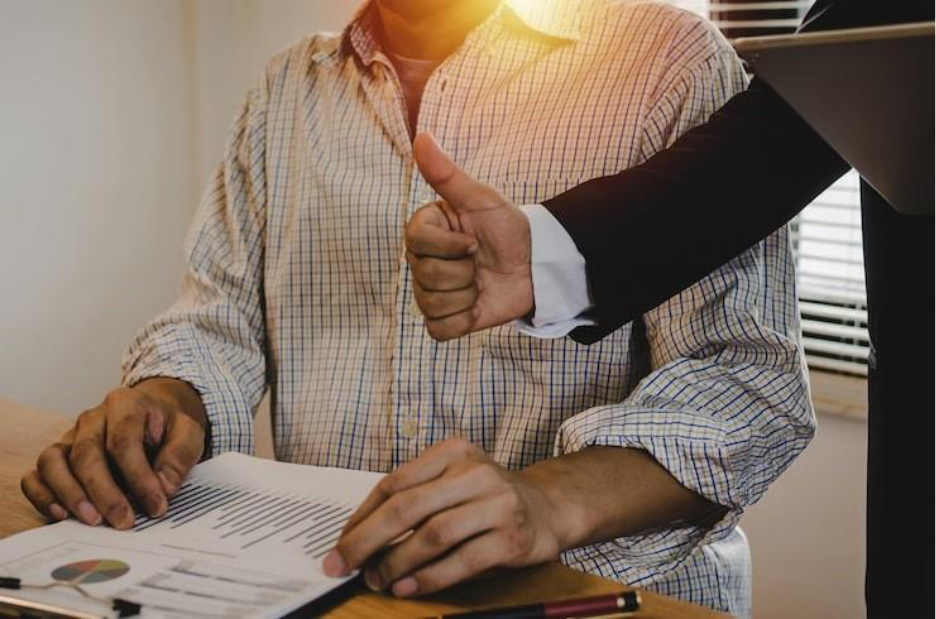 Midsection of businessman showing thumbs up to colleague on table