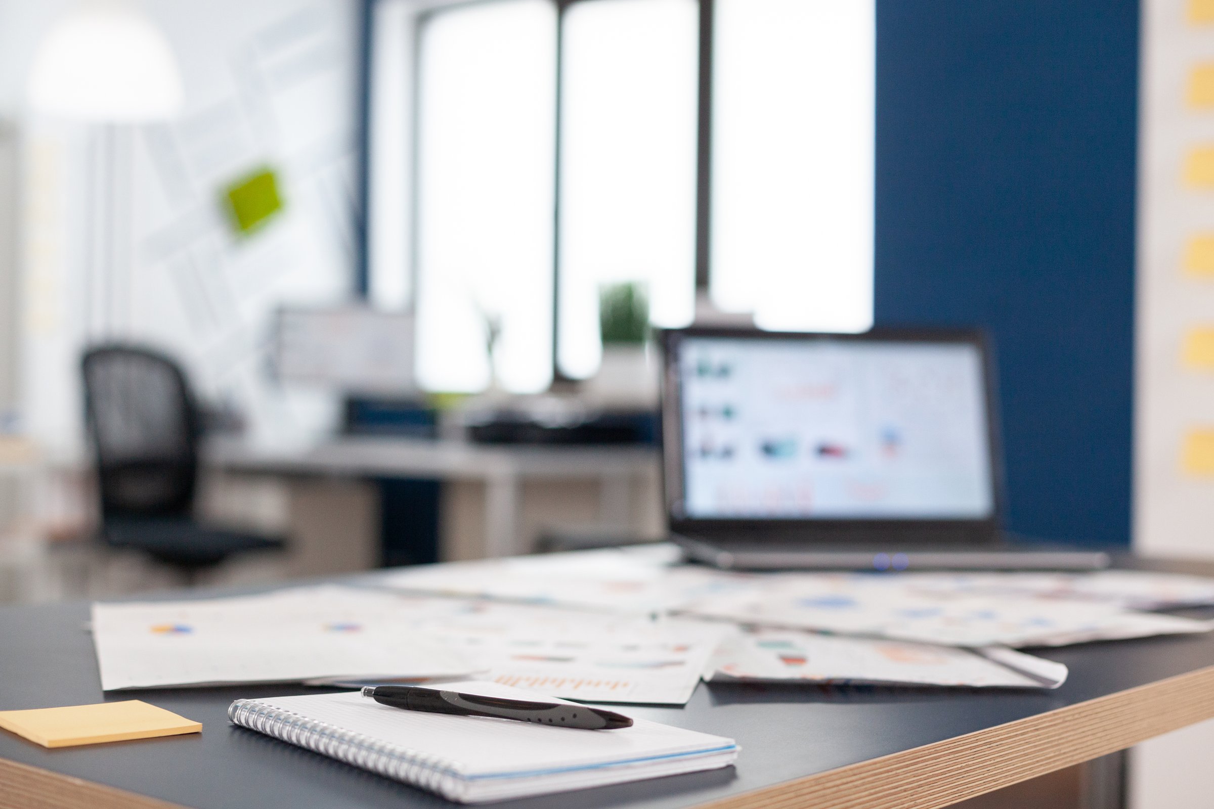 Notepad, pen, and printed analytics charts on a desk in front of a laptop in a modern office.