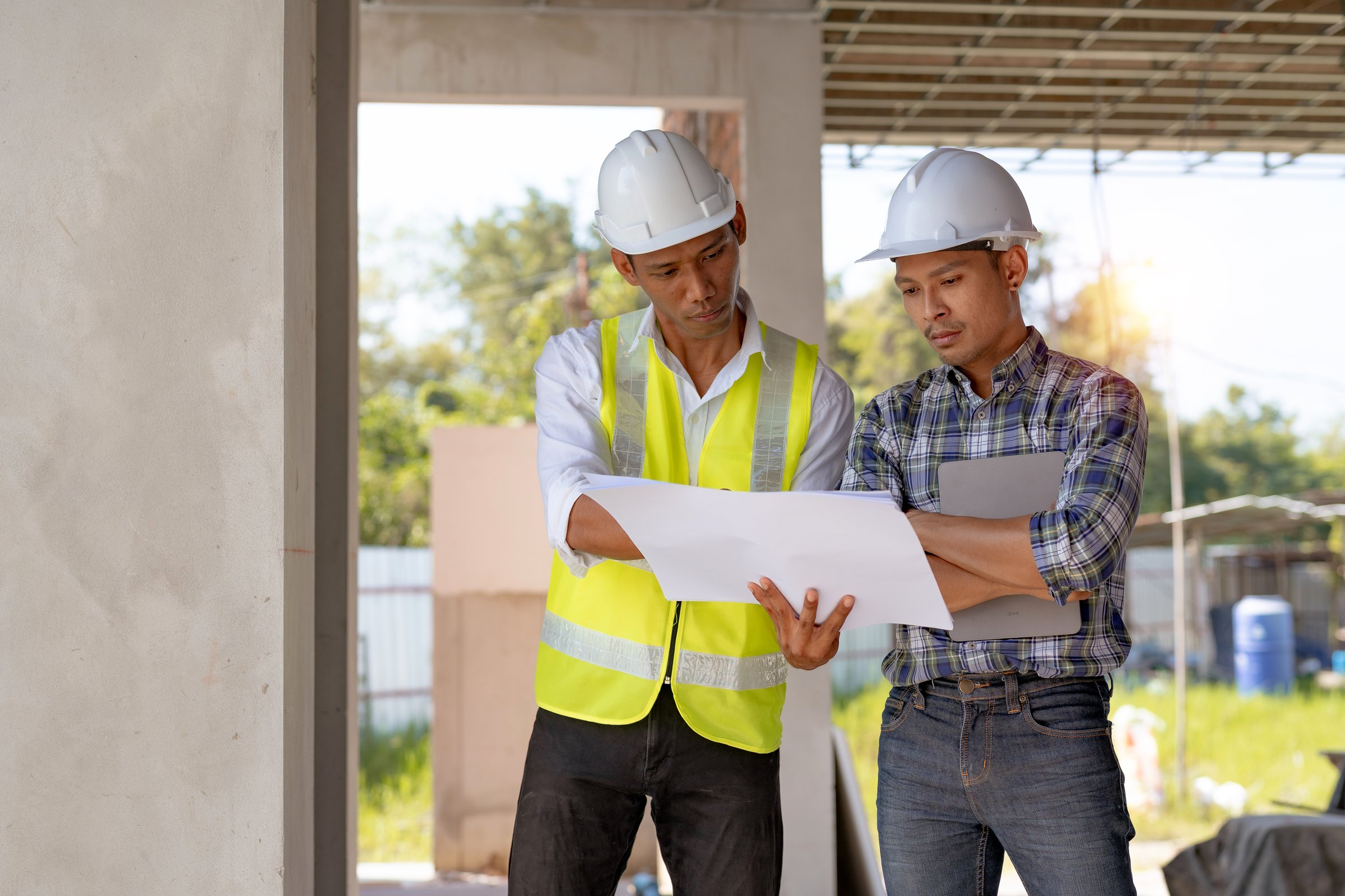 Two workers in hard hats reviewing project plans together on a job site