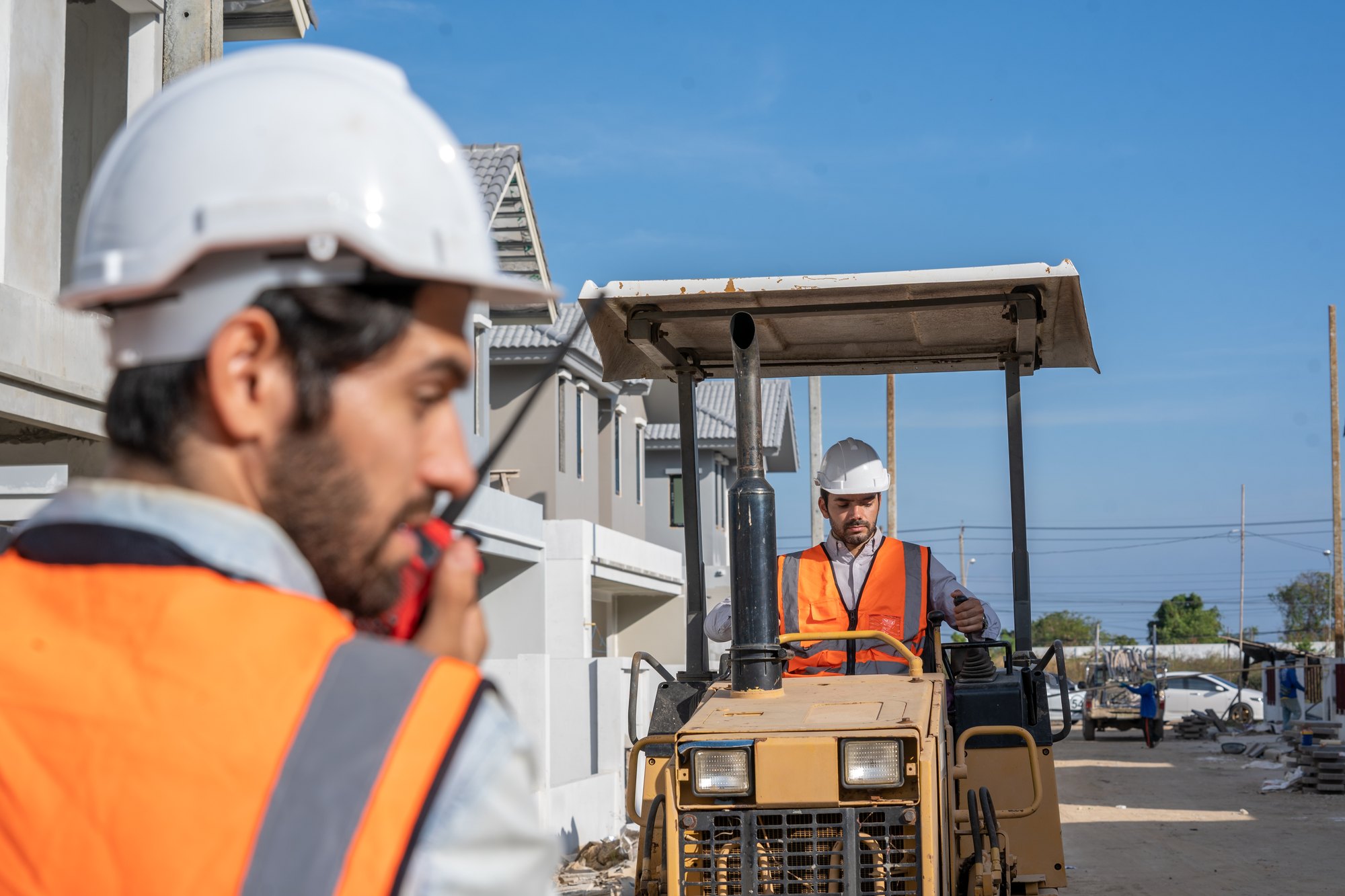 A site supervisor coordinating by radio while a contractor operates equipment on a residential construction site