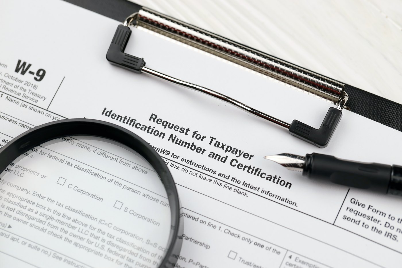 IRS Form W-9, Request for Taxpayer Identification Number and Certification, with a magnifying glass resting over the name and business name fields