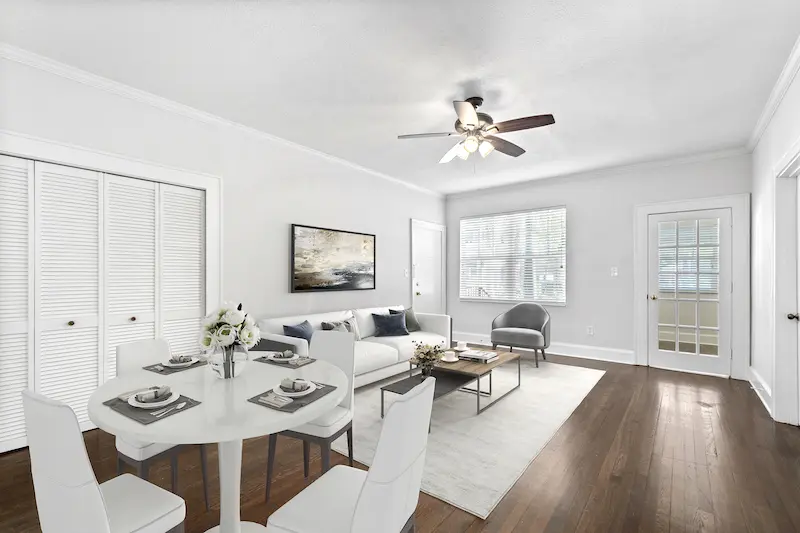 Modern open-plan living and dining room with white furniture, hardwood floors, ceiling fan, and large windows.