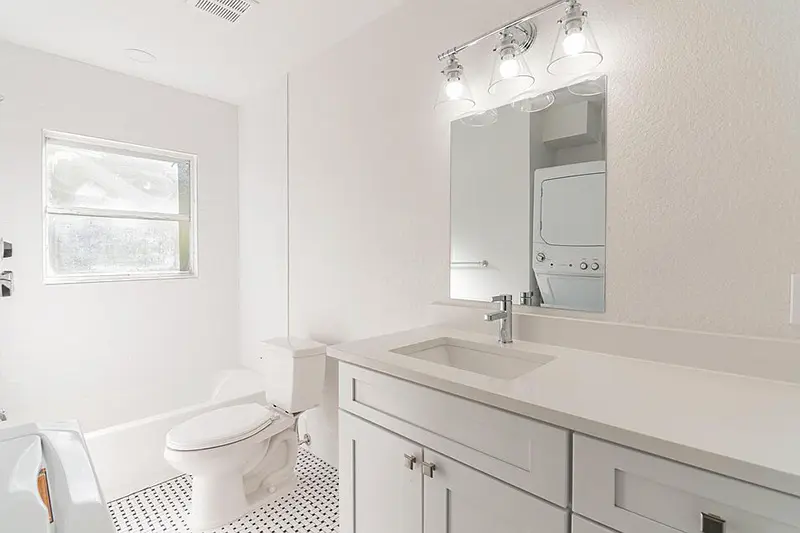 White bathroom with stacked washer/dryer in reflection of bathroom vanity mirror.