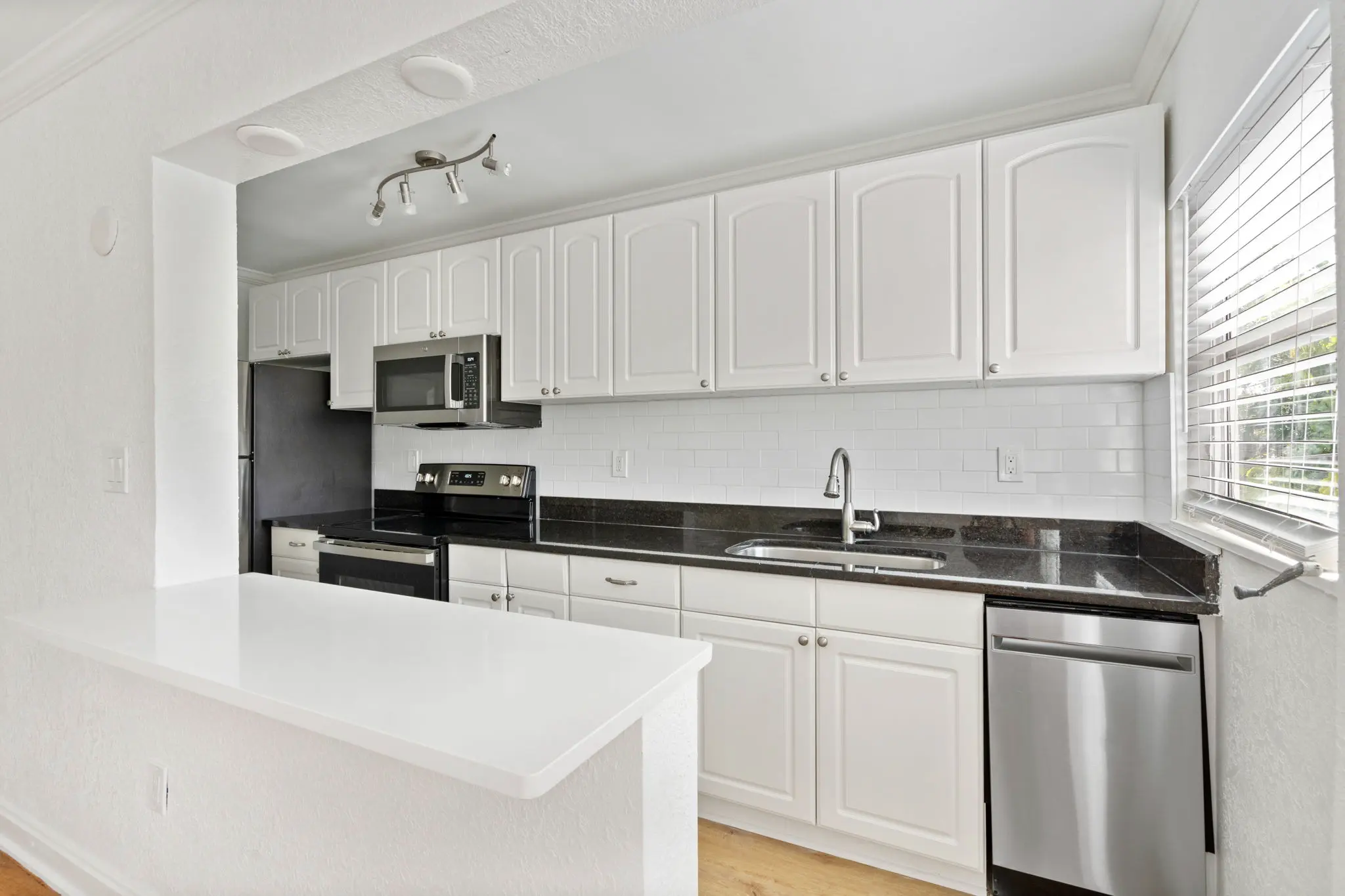 Galley kitchen with breakfast bar, white cabinets, and stainless steel appliances. 