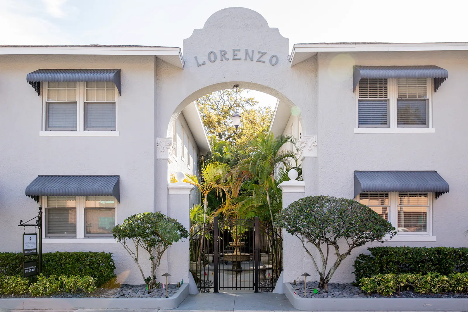 Exterior of gray building with archway overlooking a courtyard with palms, depicting the word "Lorenzo."