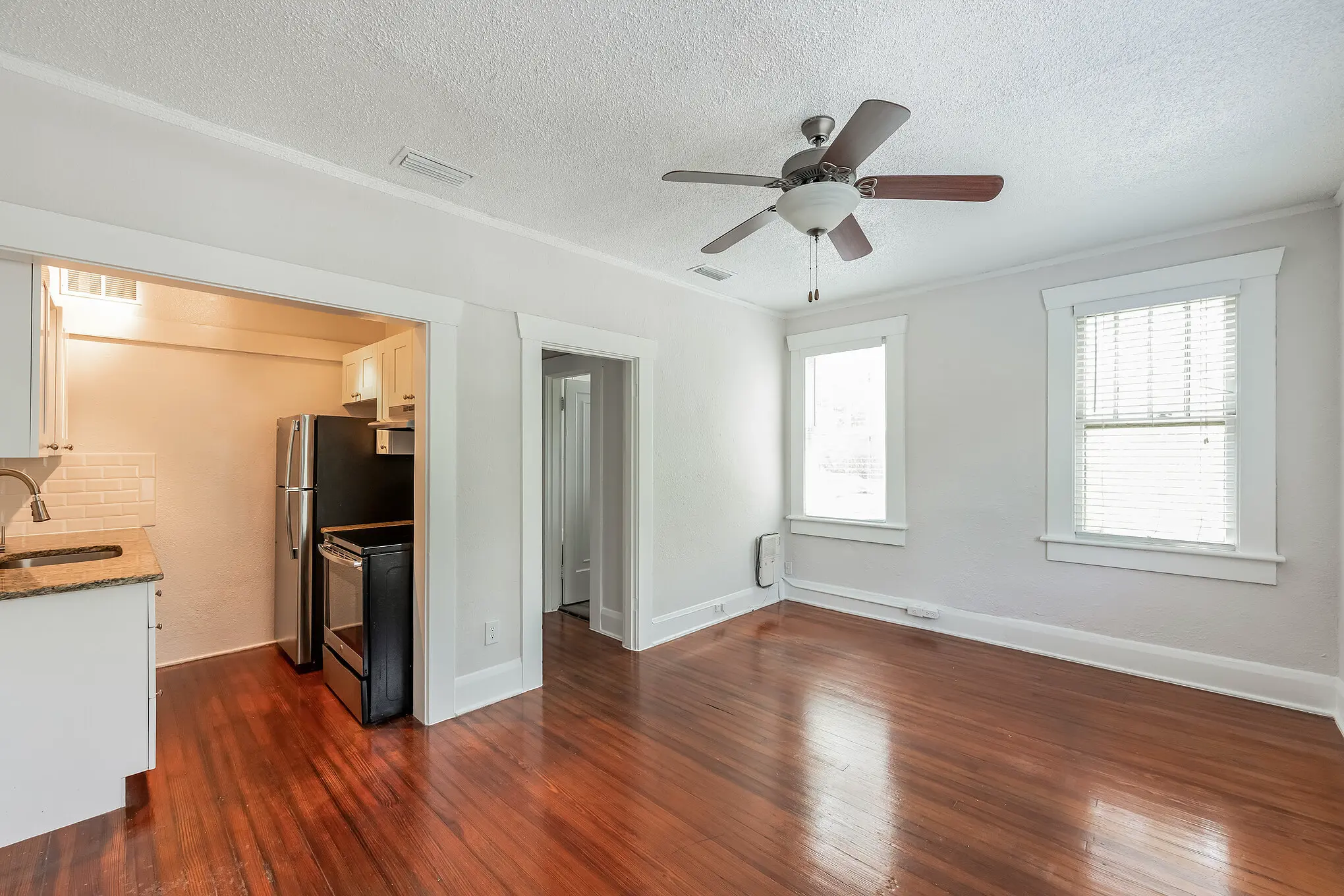 Spacious studio with wood flooring facing windows and modern galley kitchen to the left.