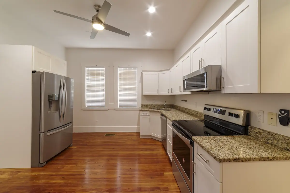 Modern kitchen with white cabinets, granite countertops, stainless steel appliances, wood flooring, and a ceiling fan.