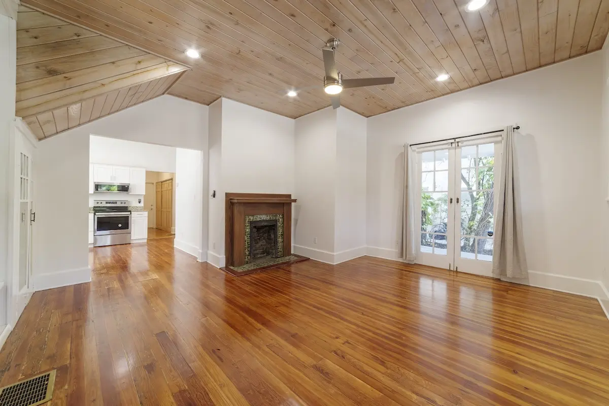 Bright living space with wood floors, wood-paneled ceiling, ceiling fan, decorative fireplace, and French doors leading outside.