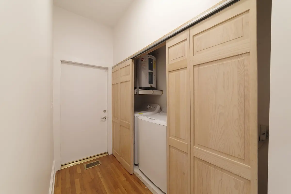 Compact laundry area with washer, dryer, and water heater tucked behind sliding wooden doors in a hallway.