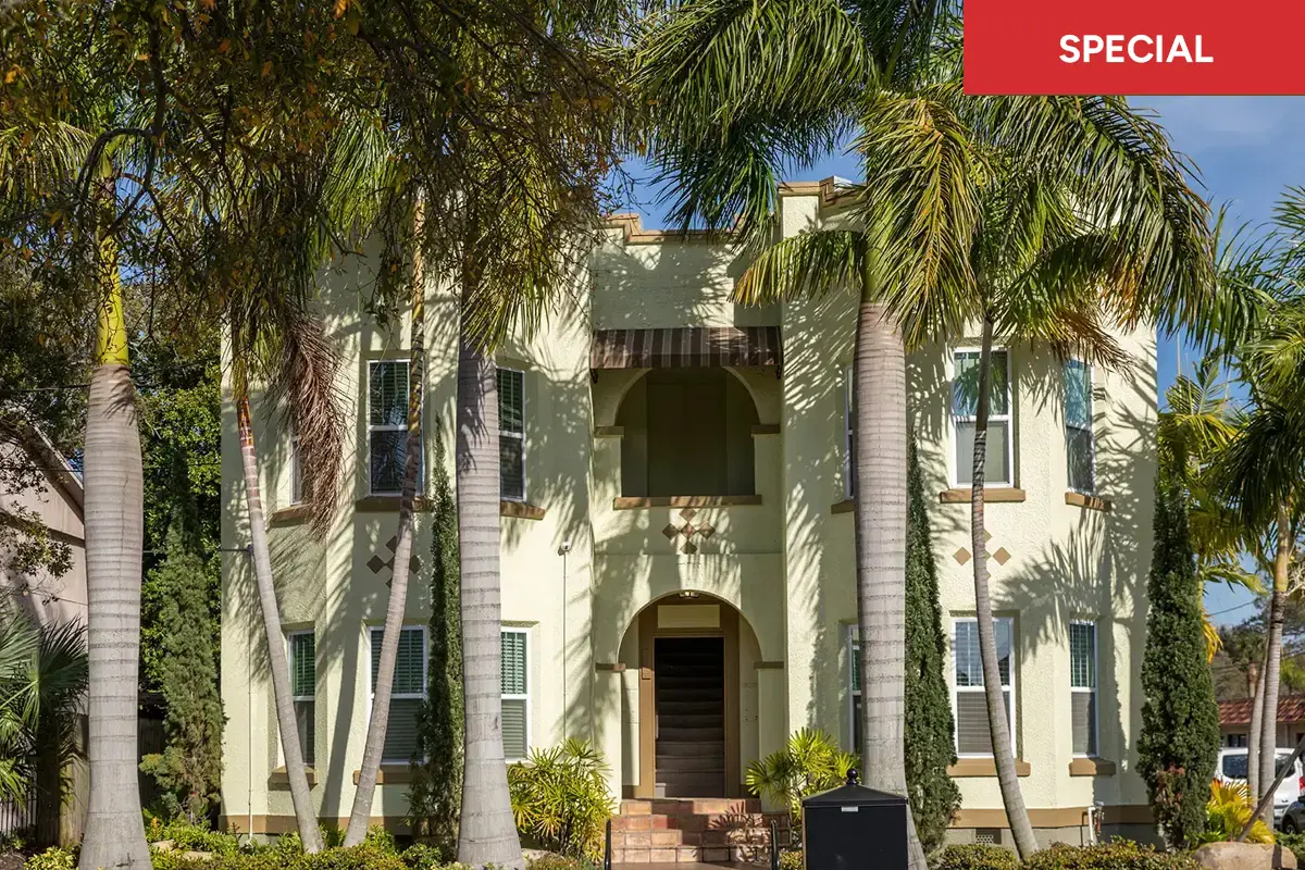 A yellow stucco apartment building surrounded by tall palm trees on a sunny day with a text overlay stating "special."