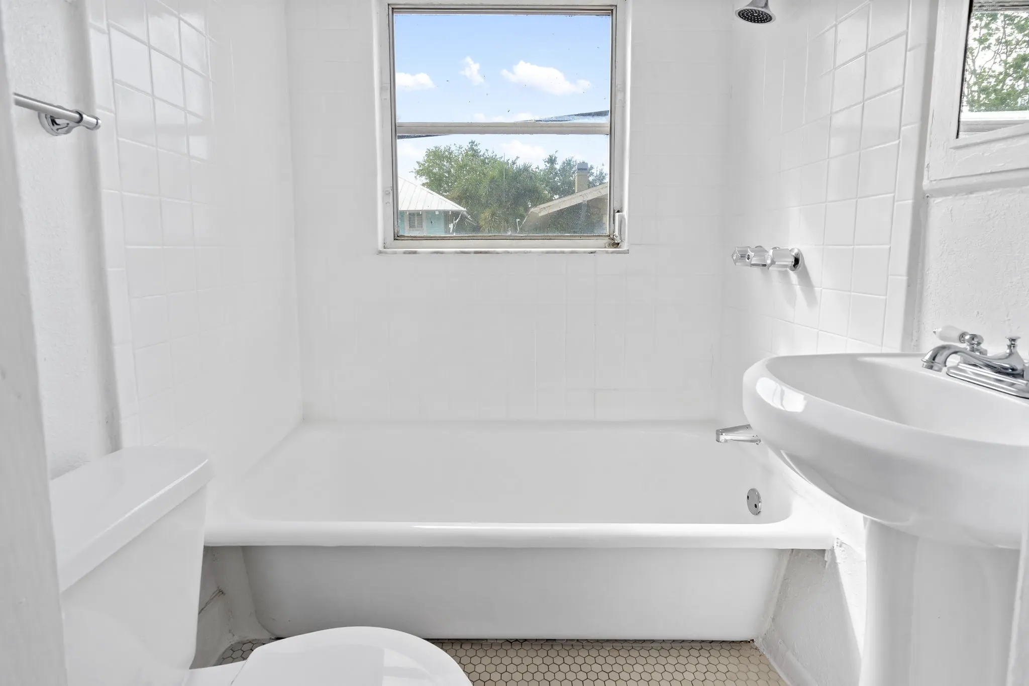 Bright white modern bathroom with a single-sink vanity, bathtub-shower combo facing bright window.