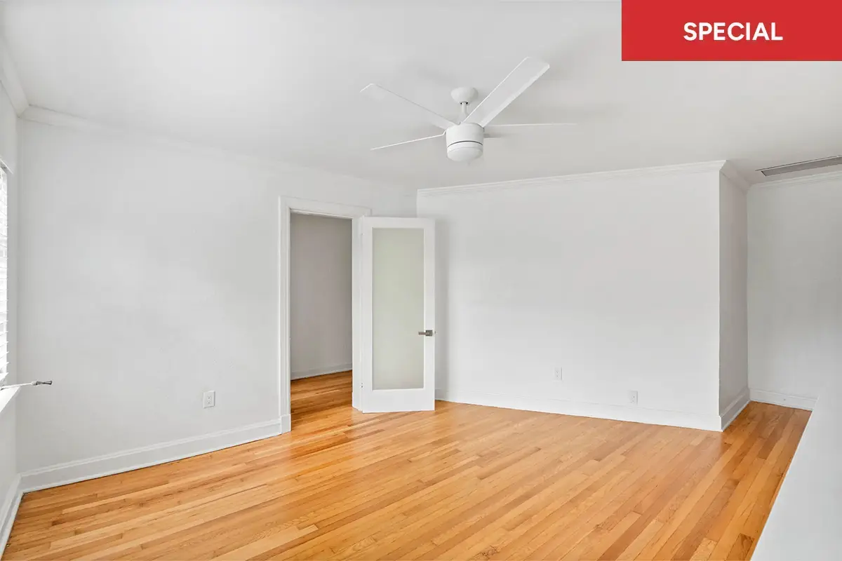 Bright, empty open-plan living area with white walls, light wood flooring, ceiling fan with light, and a small white kitchen bar with text overlay stating "SPECIAL."