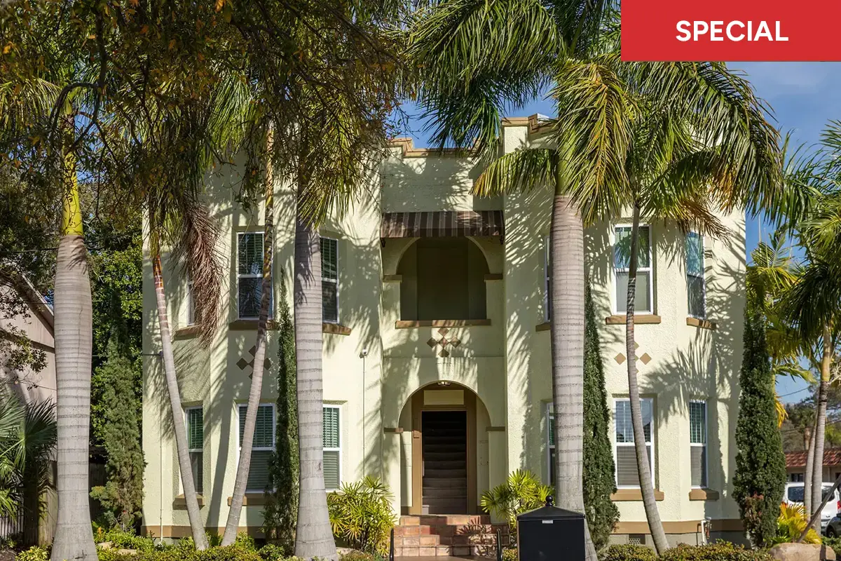 A yellow stucco apartment building surrounded by tall palm trees on a sunny day with text overlay stating "SPECIAL."