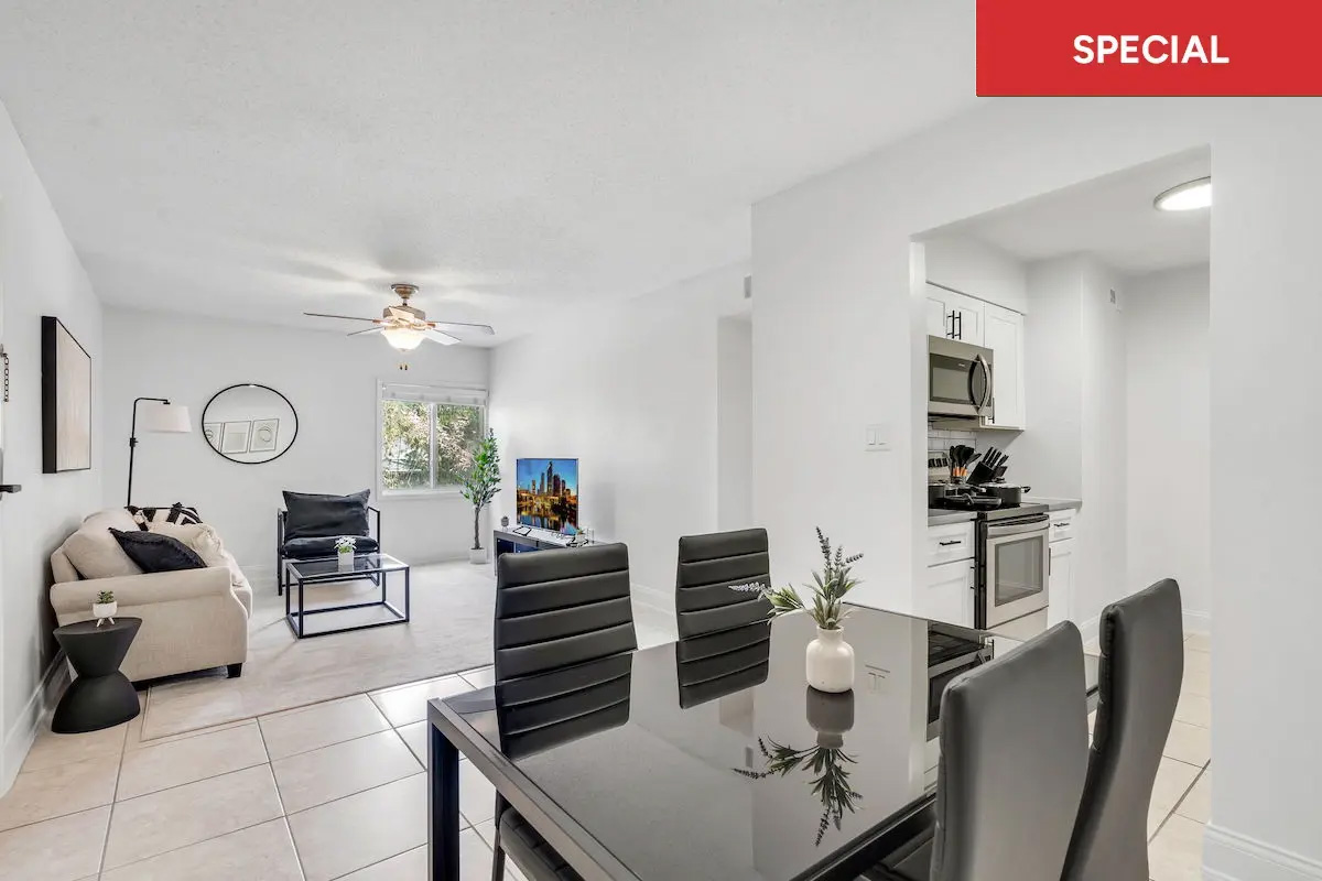 Staged dining area with modern black table, facing a living room with neutral colored furniture and kitchen to the right with red banner and text overlay stating "special."