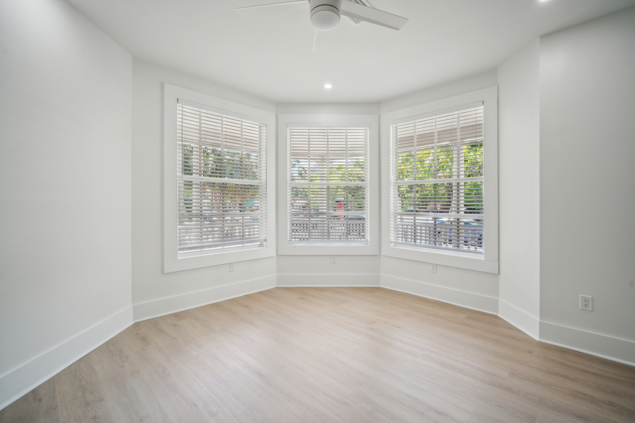Spacious living room with large bay windows facing greenery and trees.