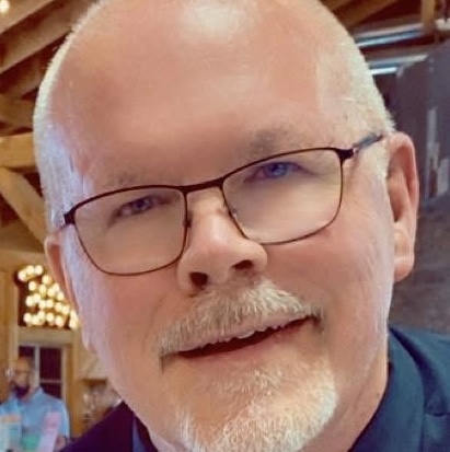 A neutral colored painting of a man with a beard and glasses smiling