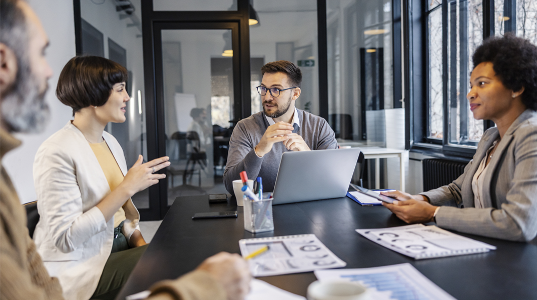 Business team having a discussion during a financial meeting in a modern office, with charts and a laptop on the table. Ask ChatGPT