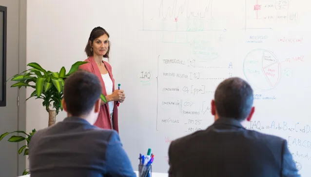 Personas atendiendo a un experto que explica conceptos de calidad de aire interior en una pizarra.