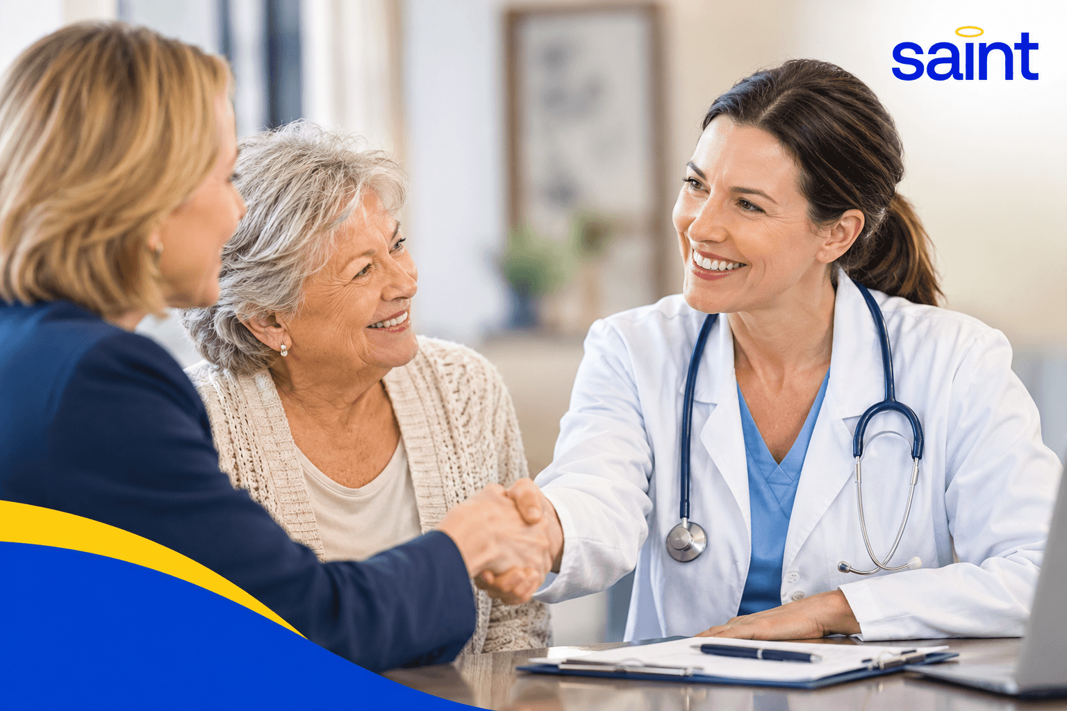 A home care professional smiles while shaking hands with a family member as an older woman looks on, representing trust, compassionate care, and positive relationships between home care providers and families. The Saint logo appears in the upper right corner.