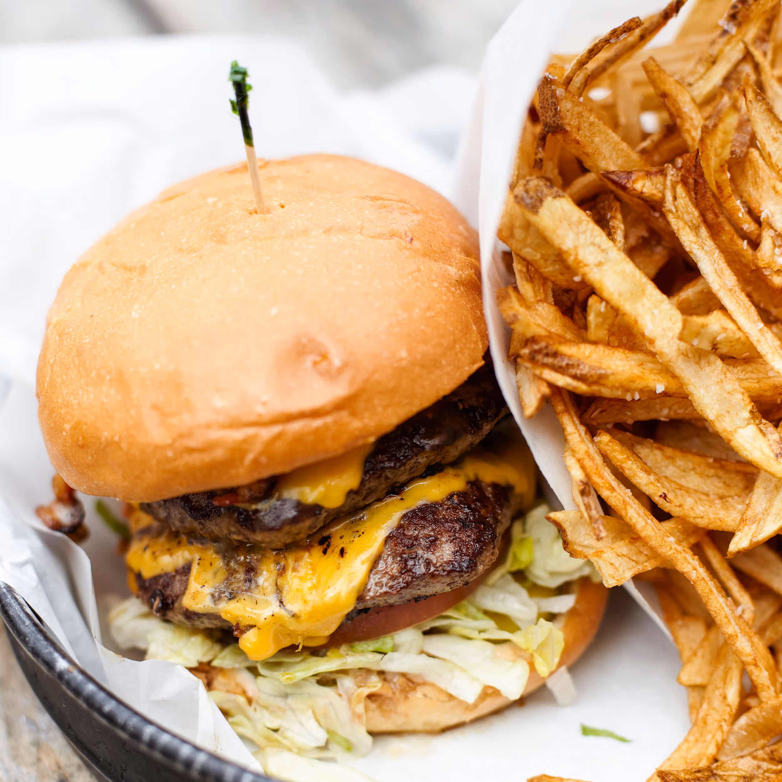 Double cheeseburger with lettuce and tomato served with a side of crispy French fries in a basket.