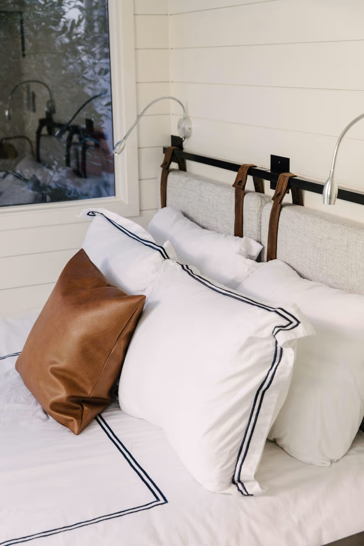 Hotel Otto bungalow interior with white bedding, navy trim, and a tan leather accent pillow