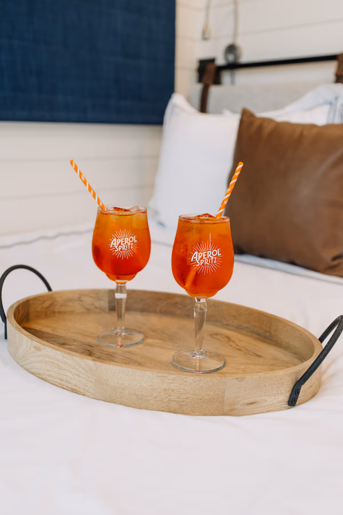 Two Aperol Spritz cocktails on a wooden tray atop a freshly made bed at Hotel Otto
