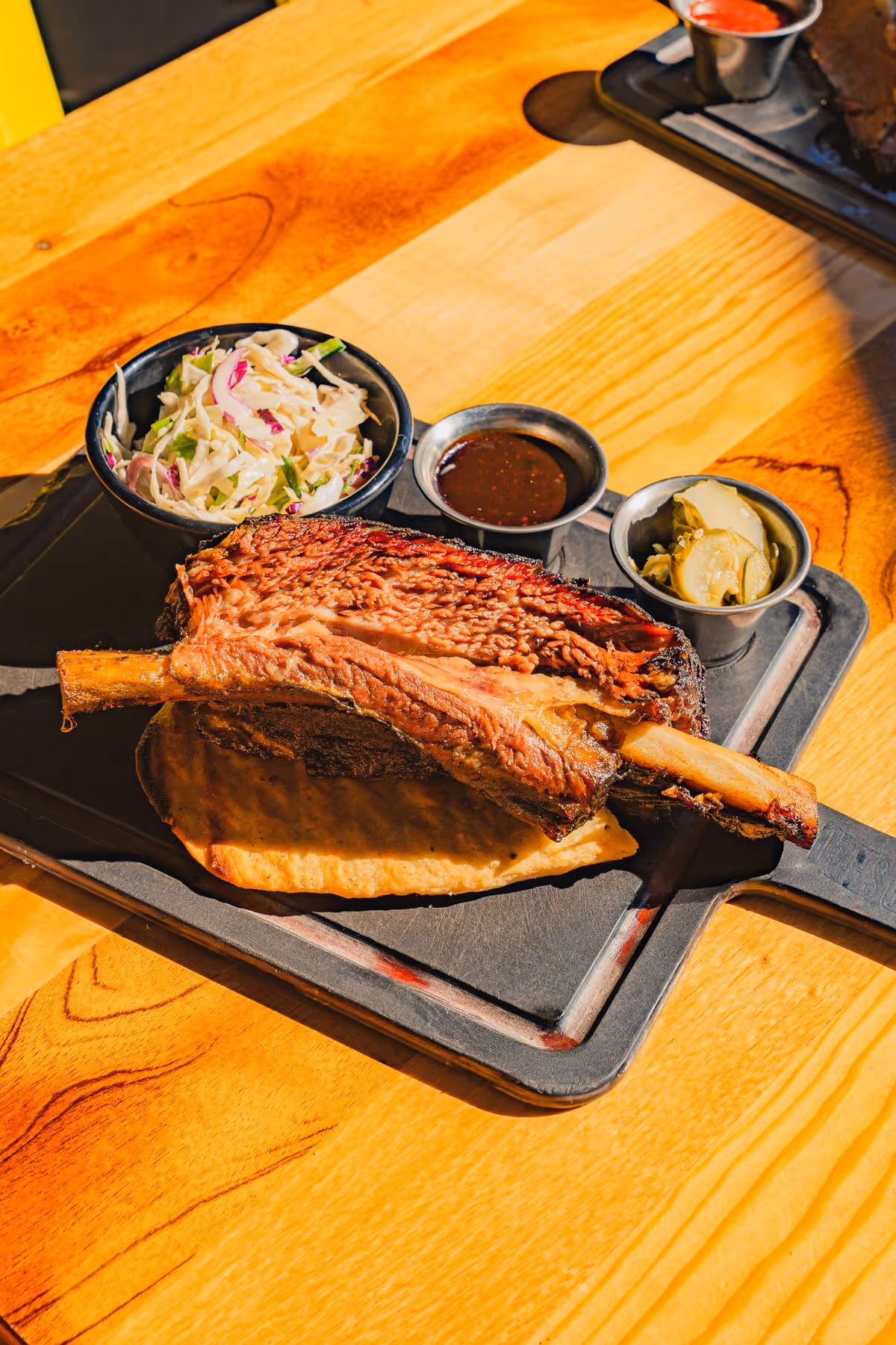 Massive smoked beef rib on a black tray with slaw, pickles, and Texas barbecue sauce at Love's