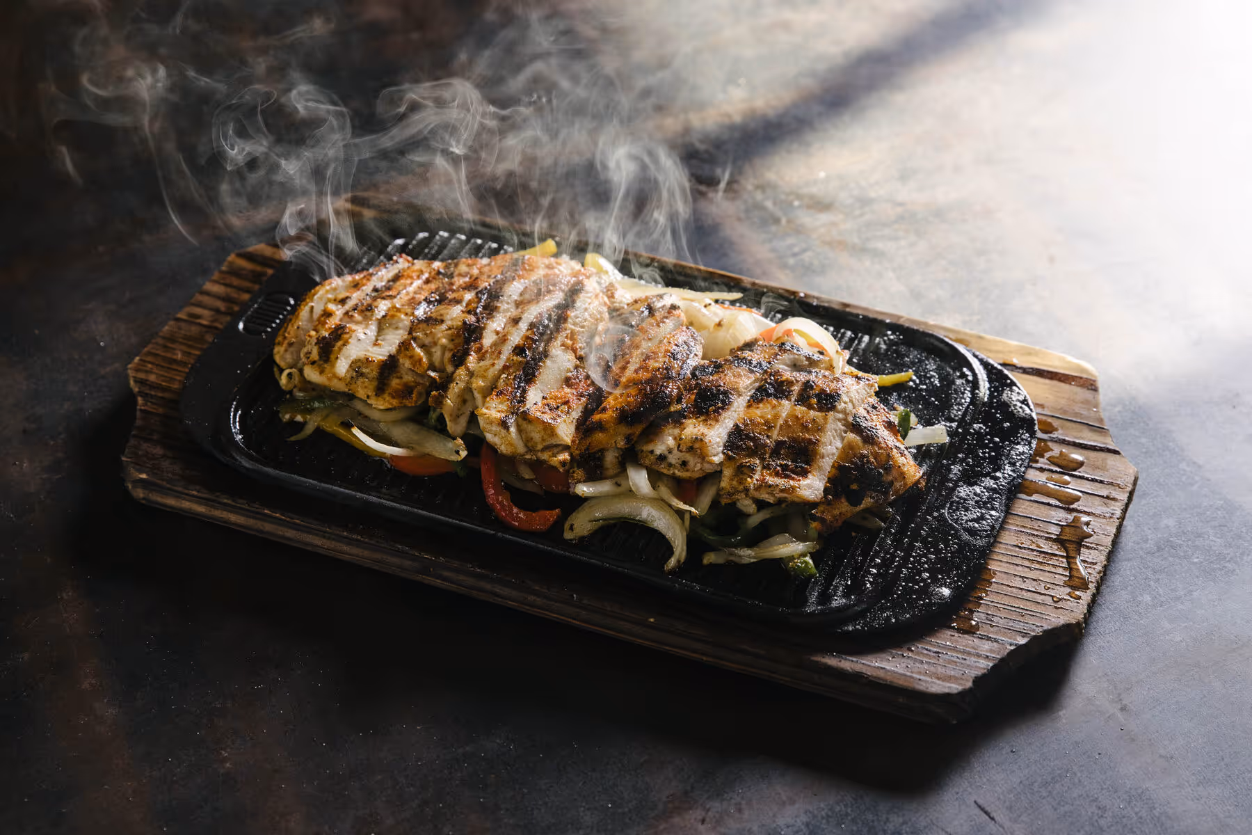 Sizzling grilled chicken fajitas over peppers and onions on a cast iron platter