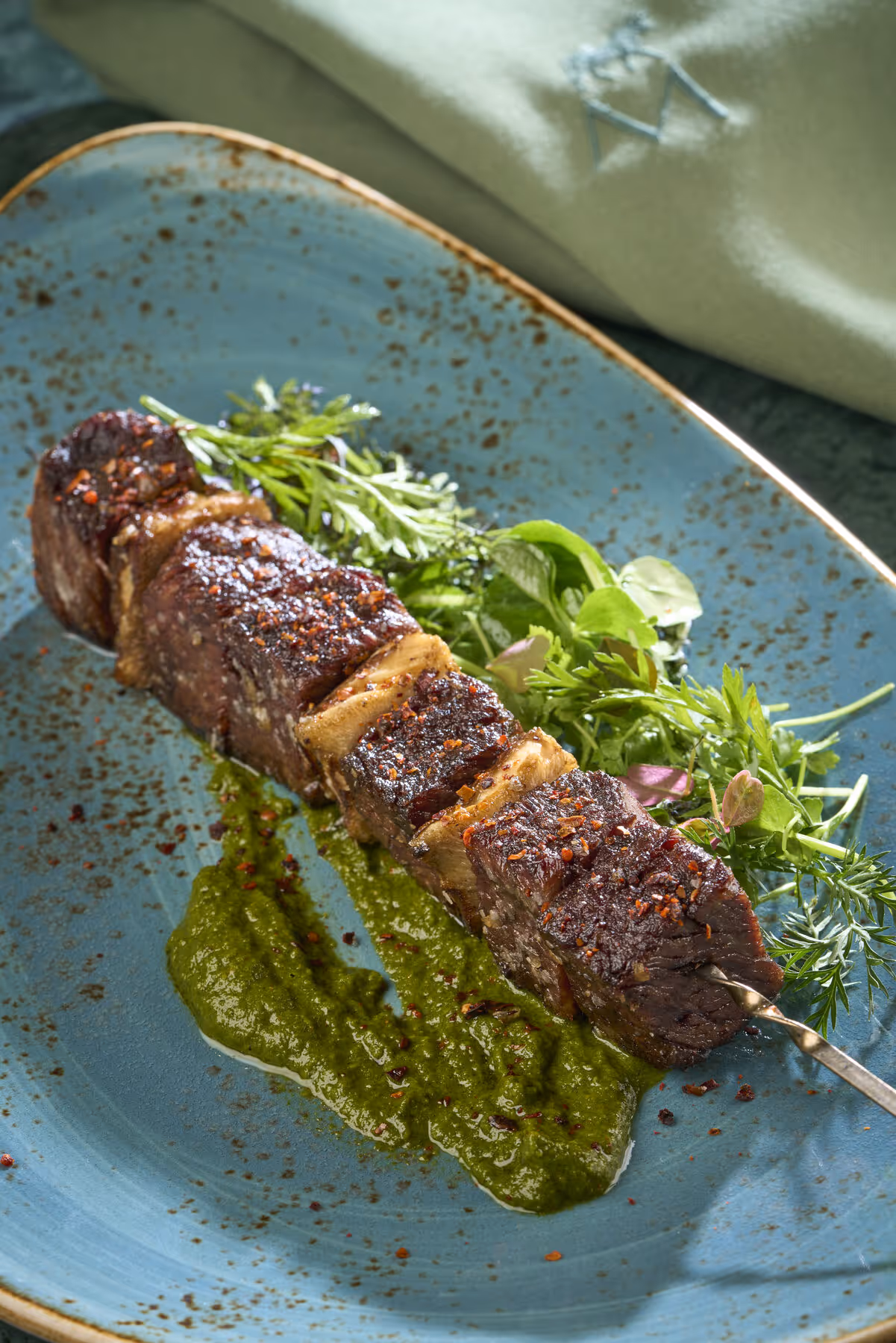Char-grilled short rib skewer dusted with chili flakes over a chimichurri at Meraki