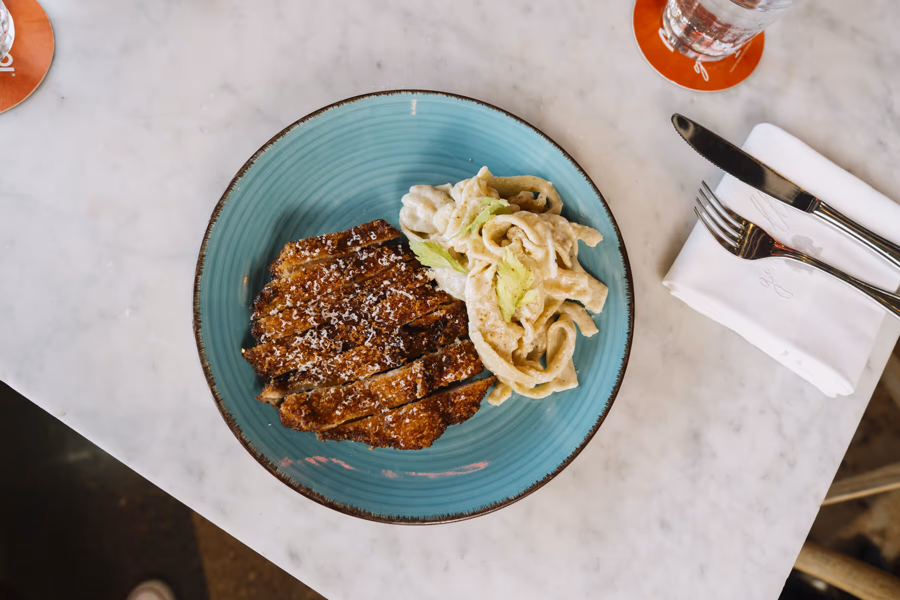 Crispy chicken milanese over creamy fettuccine on an aqua ceramic plate at Gemelle