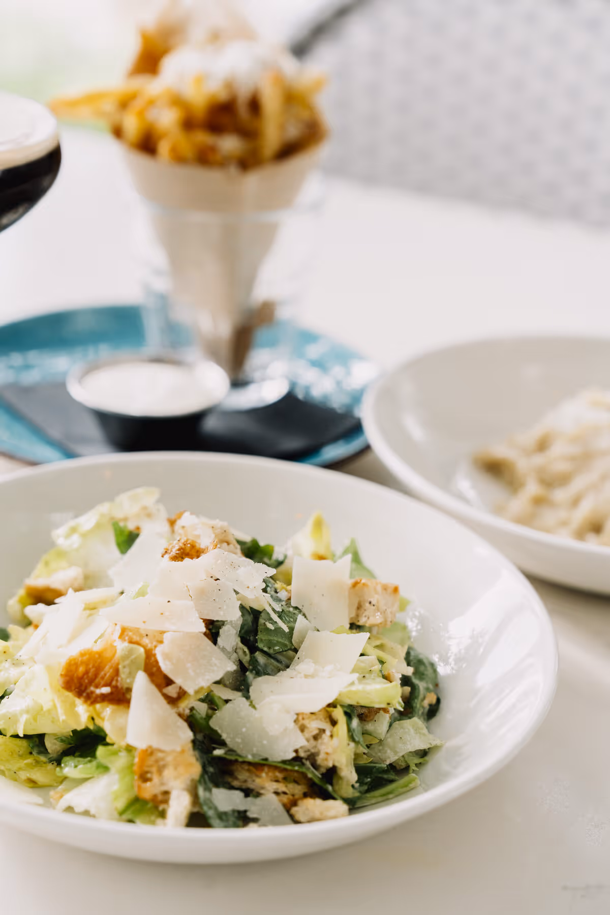 Caesar salad with shaved parmigiano and grilled chicken alongside a cone of fries at Gemelle