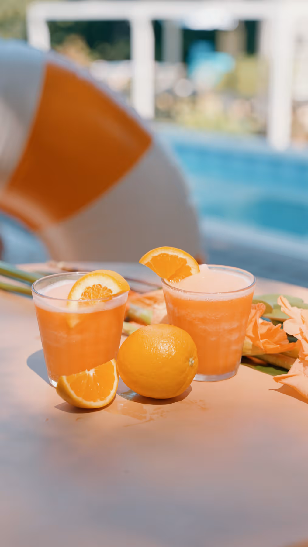 Two frozen citrus cocktails poolside with orange and lemon garnishes