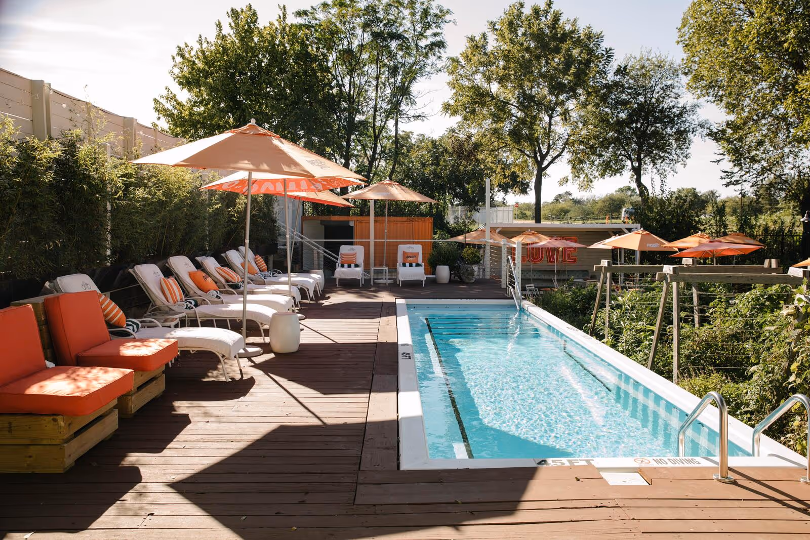 Hotel Otto pool deck with orange Aperol umbrellas, white chaise lounges, and a glowing LOVE neon sign at sunset