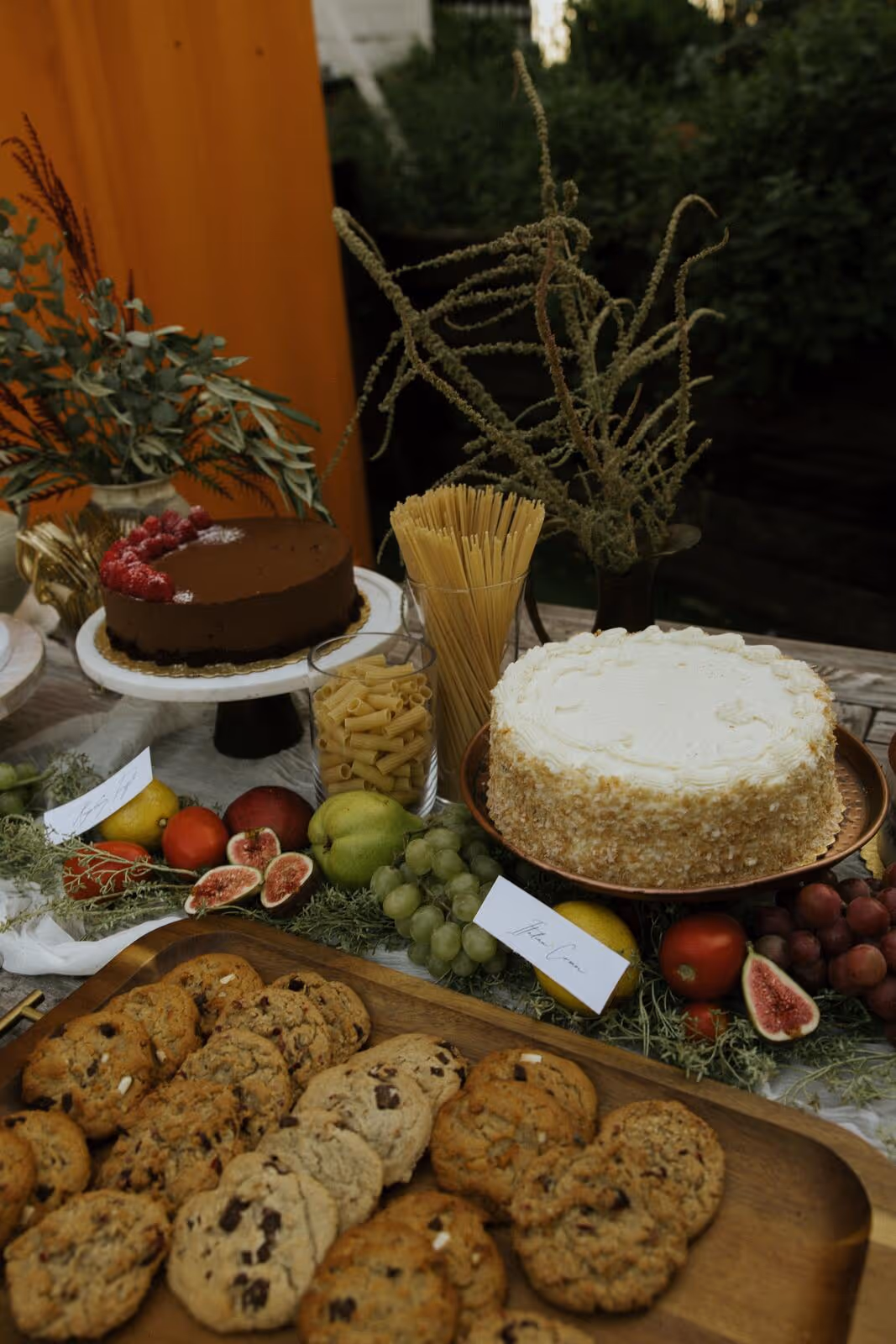 Dessert spread at a private event with chocolate raspberry tart, vanilla cake, fresh fruit, and chocolate chip cookies on a wooden table