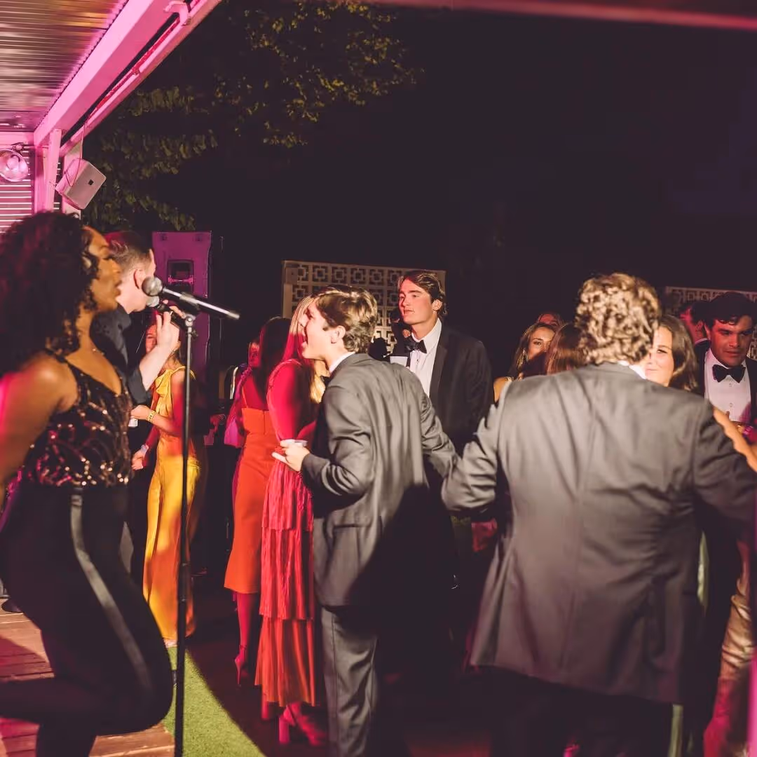 Live singer performing under pink lights as guests in formal attire dance and mingle at an evening event