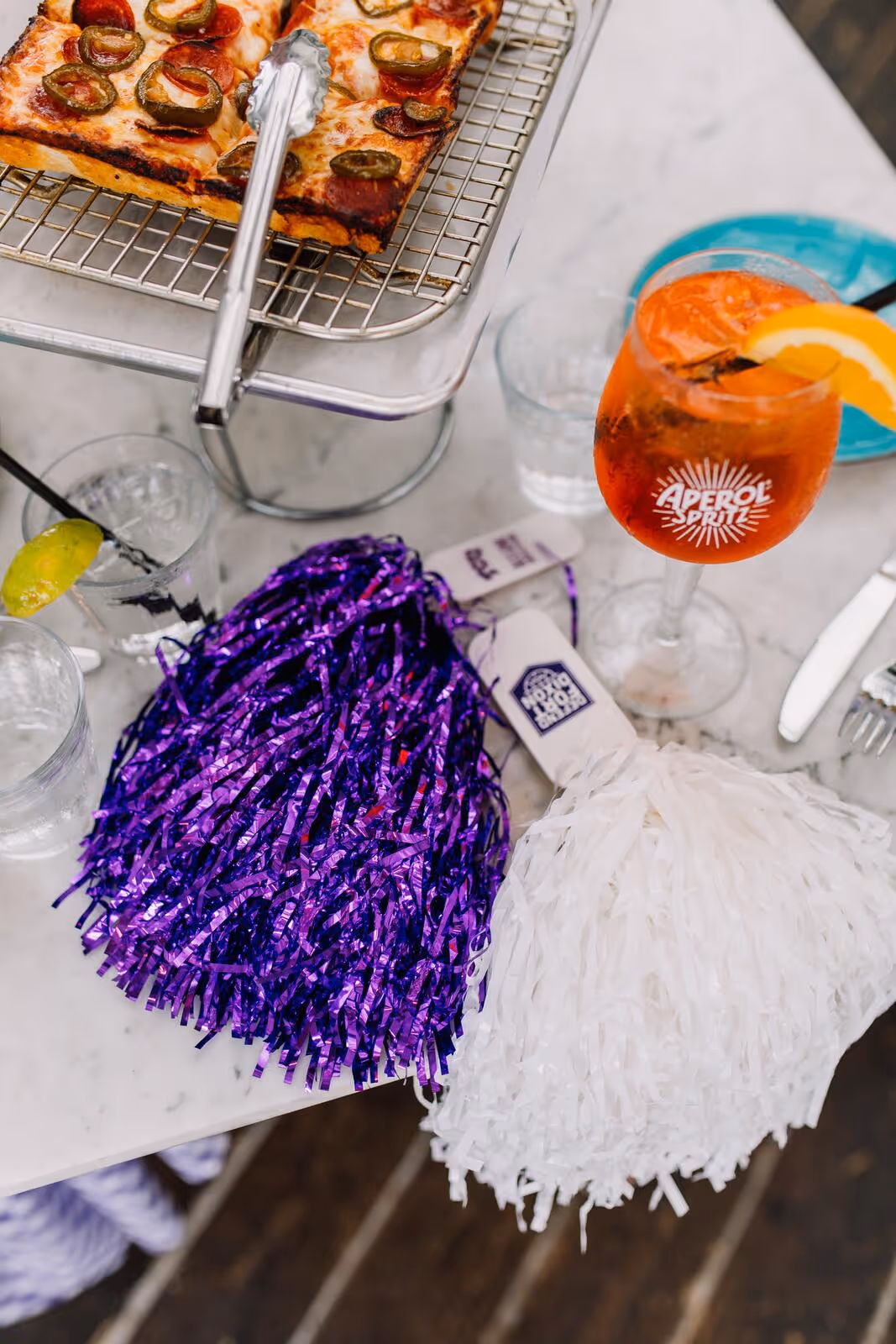 Detroit-style pizza, an Aperol Spritz, and TCU purple-and-white pom-poms staged for a game day private event